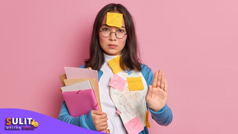 A female Asian with glasses and various stickers all around her in a stop hand sign.